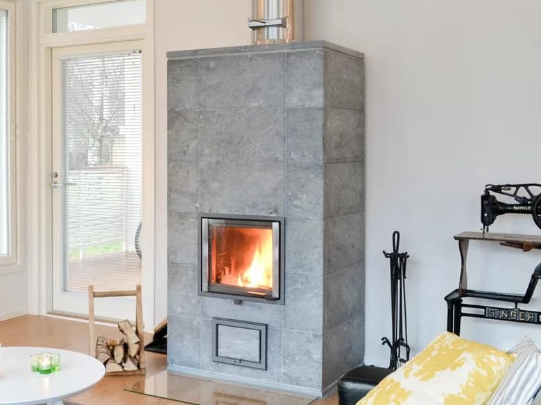 Freistehender Specksteinofen aus großformatigen Natursteinplatten mit brennendem Feuer in einem hellen Wohnraum