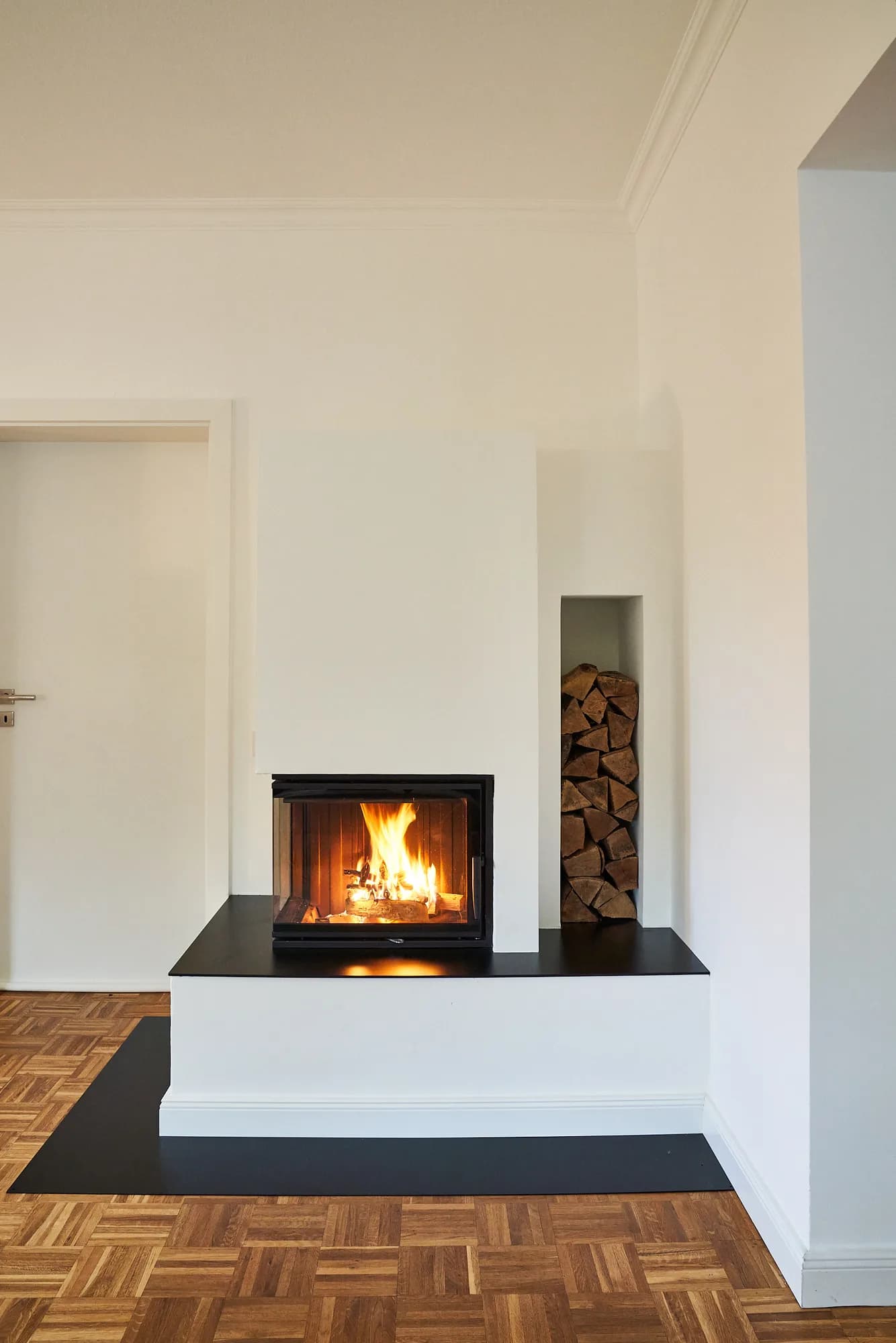 Kamineinbau in weißer Wand mit brennendem Feuer und danebenliegender Holznische