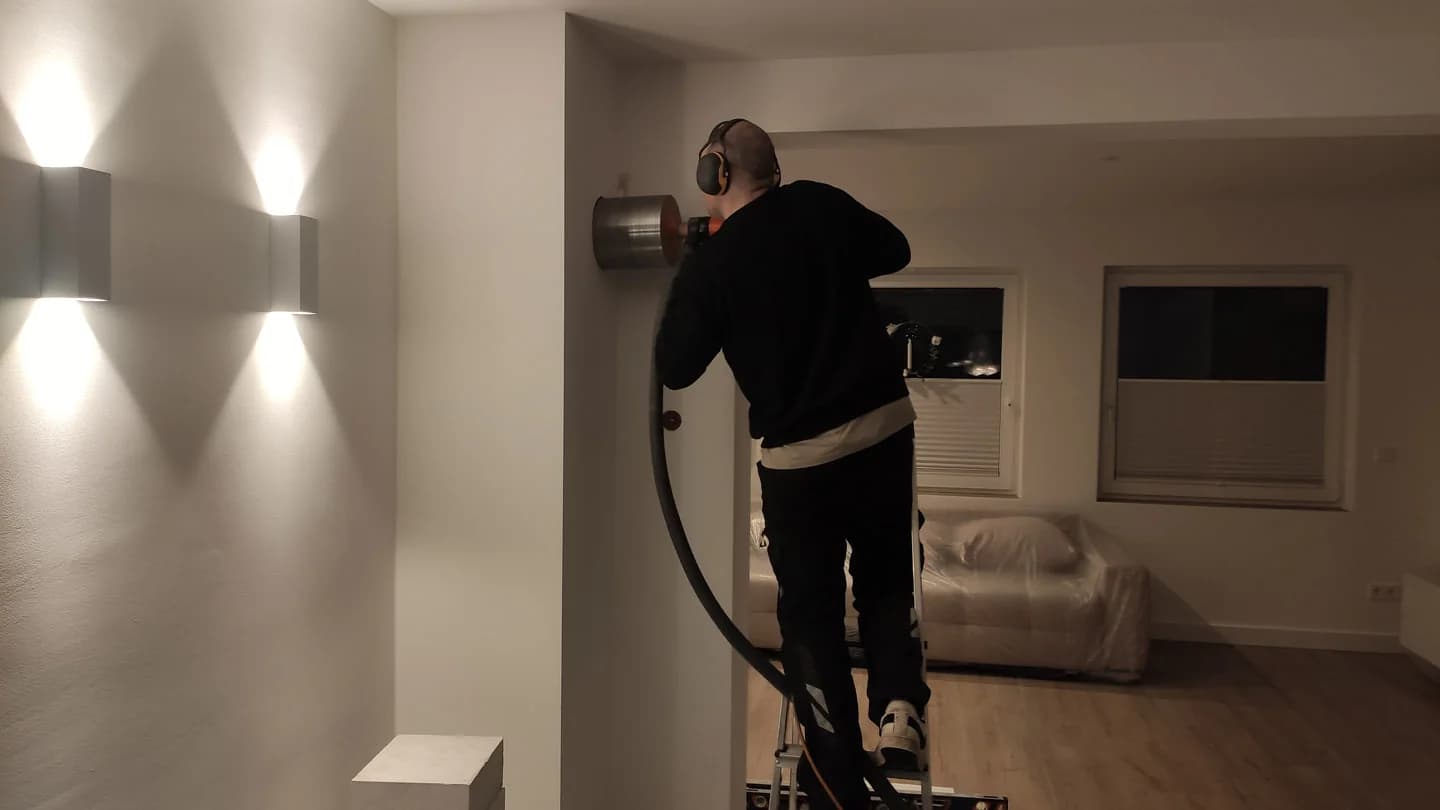 Handwerker auf einer Leiter setzt eine Wanddurchführung mit Leitung